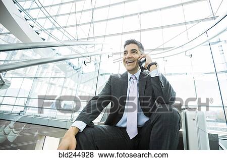 Stock Photo - Smiling Mixed Race businessman sitting on staircase talking on cell phone. Fotosearch