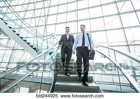 Stock Photography - Smiling Mixed Race businessmen descending staircase. Fotosearch