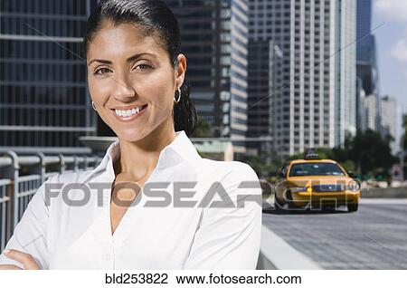 Stock Image - Smiling Mixed Race businesswoman near taxi in city. Fotosearch