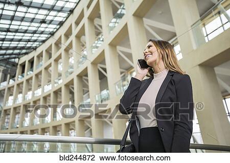 Stock Image - Smiling Mixed Race businesswoman talking on cell phone in lobby. Fotosearch