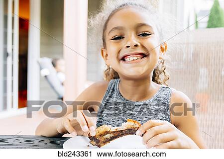 Stock Image - Smiling Mixed Race girl eating rib outdoors. Fotosearch