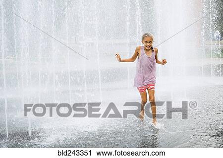 Stock Image - Smiling Mixed Race girl running fountain. Fotosearch