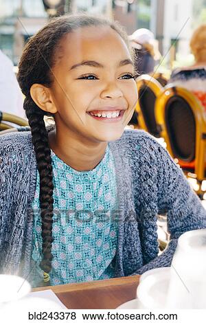 Stock Photo - Smiling Mixed Race girl sitting at restaurant table. Fotosearch