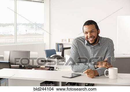 Picture - Smiling Mixed Race man leaning in office. Fotosearch