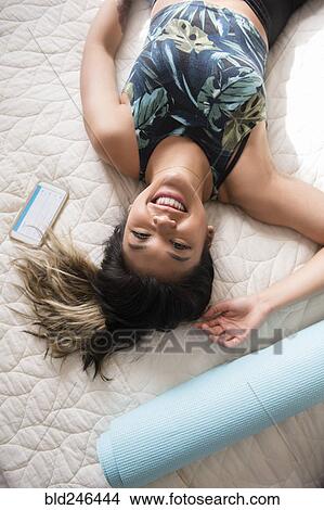 Picture - Smiling Mixed Race woman laying on bed resting after workout. Fotosearch