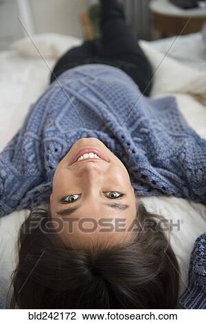 Stock Image - Smiling Mixed Race woman laying on bed. Fotosearch
