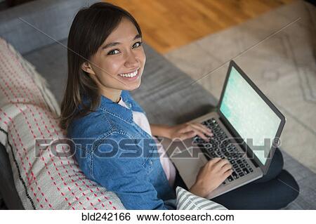 Smiling Mixed Race woman using laptop on sofa View Large Photo Image Stock Photograph - Smiling Mixed Race woman using laptop on sofa. Fotosearch