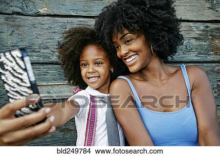 Picture - Smiling mother and daughter posing for cell phone selfie. Fotosearch