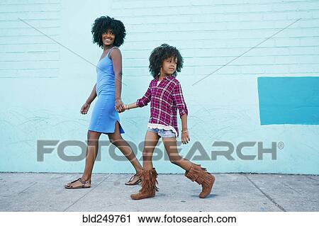 Stock Image - Smiling mother and daughter walking on sidewalk. Fotosearch