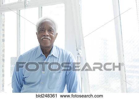 Stock Image - Smiling older Black man near the window. Fotosearch