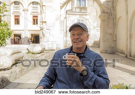 Stock Photo - Smiling older Caucasian man drinking coffee in garden. Fotosearch