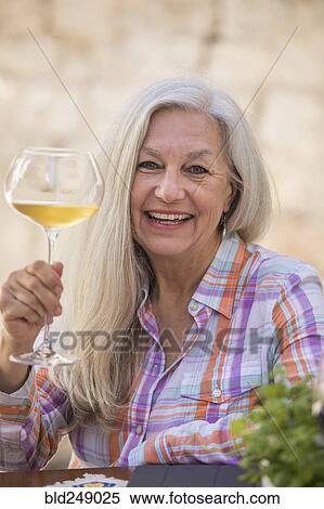 Stock Photography - Smiling older Caucasian woman holding white wine. Fotosearch