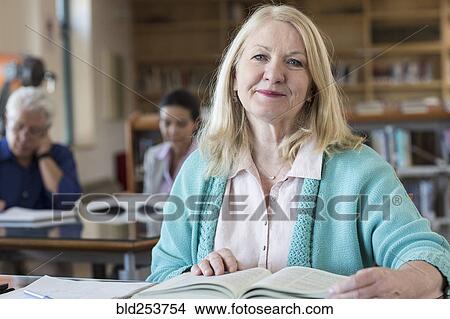 Picture - Smiling older woman reading book in library. Fotosearch