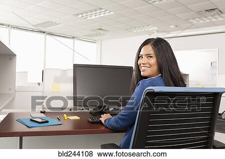 Stock Photo - Smiling Pacific Islander woman using computer in office. Fotosearch