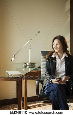 Smiling Thai businesswoman holding cell phone in office View Large Photo Image Stock Image - Smiling Thai businesswoman holding cell phone in office. Fotosearch