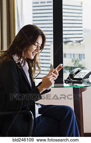 Smiling Thai businesswoman texting on cell phone in office View Large Photo Image Stock Photo - Smiling Thai businesswoman texting on cell phone in office. Fotosearch