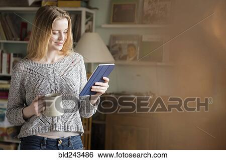 Stock Photograph - Smiling woman drinking coffee and using digital tablet. Fotosearch