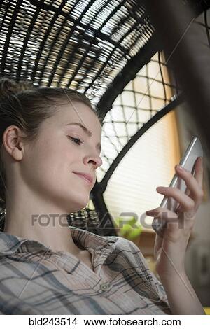 Smiling woman in wicker chair texting on cell phone View Large Photo Image Picture - Smiling woman in wicker chair texting on cell phone. Fotosearch