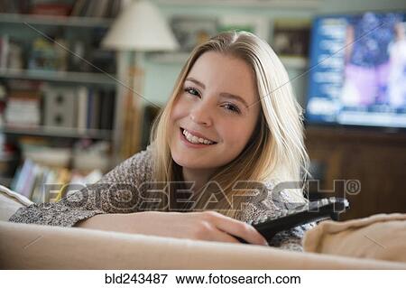Stock Photo - Smiling woman leaning on sofa holding remote control. Fotosearch
