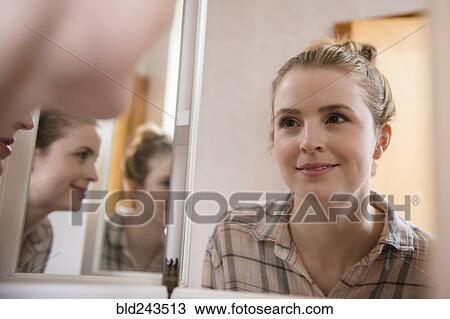 Stock Image - Smiling woman looking in mirror. Fotosearch