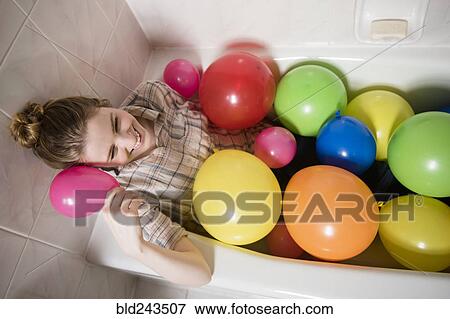 Stock Photo - Smiling woman sitting in bathtub with multicolor balloons. Fotosearch