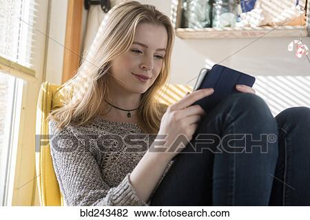 Stock Image - Smiling woman sitting near window using digital tablet. Fotosearch