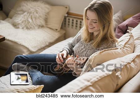 Smiling woman sitting on sofa playing ukulele View Large Photo Image Stock Photography - Smiling woman sitting on sofa playing ukulele. Fotosearch
