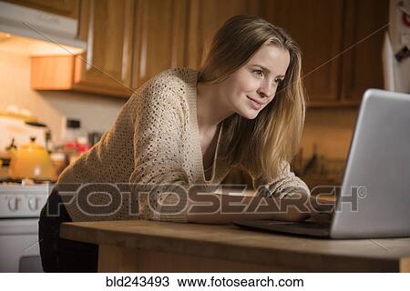 Smiling woman using laptop in domestic kitchen View Large Photo Image Stock Image - Smiling woman using laptop in domestic kitchen. Fotosearch