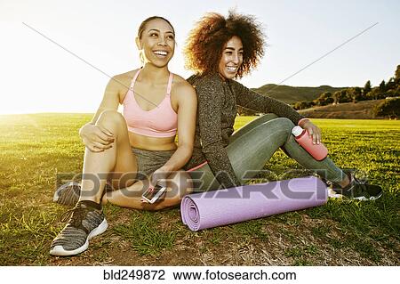 Stock Image - Smiling women sitting in sunny field. Fotosearch