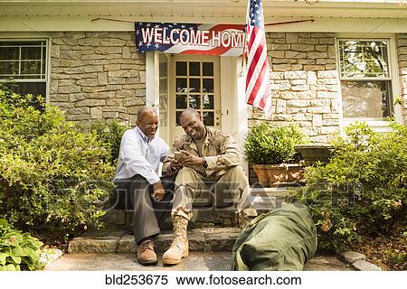 Stock Photography - Soldier and father sitting on front stoop texting on cell phone. Fotosearch
