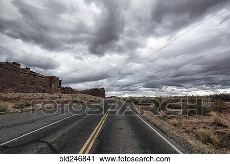 Stock Image - Street in desert under clouds. Fotosearch