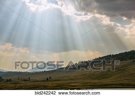 Stock Image - Sunbeams shining through clouds over rolling rural landscape. Fotosearch