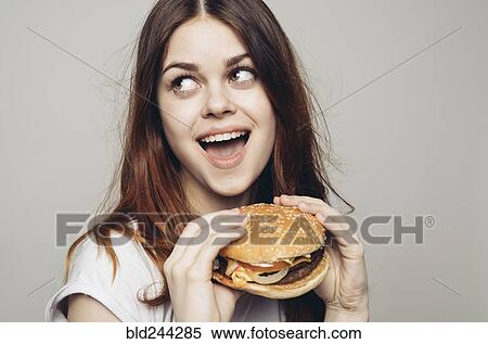 Stock Photography - Surprised Caucasian woman holding cheeseburger. Fotosearch