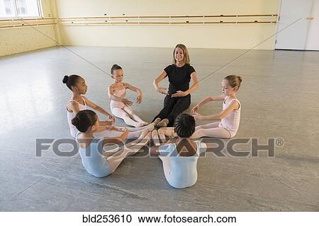 Stock Image - Teacher and students sitting on floor in ballet studio. Fotosearch