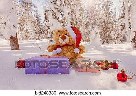 Stock Image - Teddy bear with Christmas gifts and ornaments in snow. Fotosearch