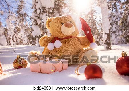 Stock Image - Teddy bear with Christmas gifts and ornaments in snow. Fotosearch