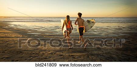 Stock Photo - Teenage boy and girl carrying surfboards running to ocean. Fotosearch