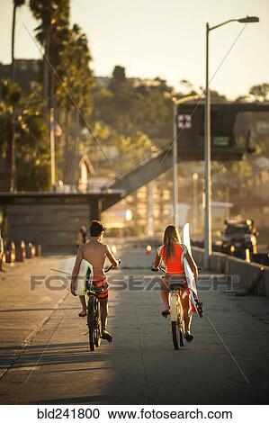 Teenage boy and girl riding bicycles carrying surfboards View Large Photo Image Stock Image - Teenage boy and girl riding bicycles carrying surfboards. Fotosearch