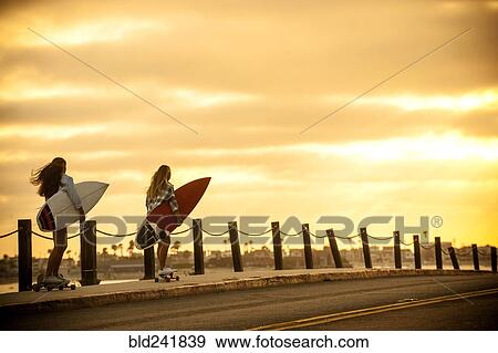 Stock Photo - Teenage girls carrying surfboards on skateboards. Fotosearch