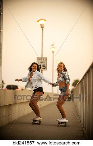Stock Photo - Teenage girls holding hands while riding skateboards. Fotosearch