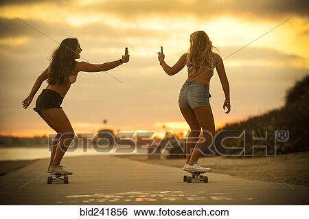 Stock Photograph - Teenage girls riding skateboards holding cell phones. Fotosearch