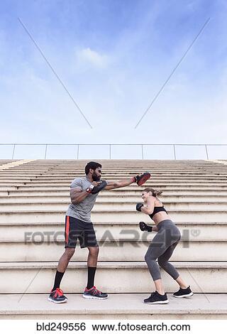 Stock Photograph - Trainer and woman boxing on bleachers. Fotosearch