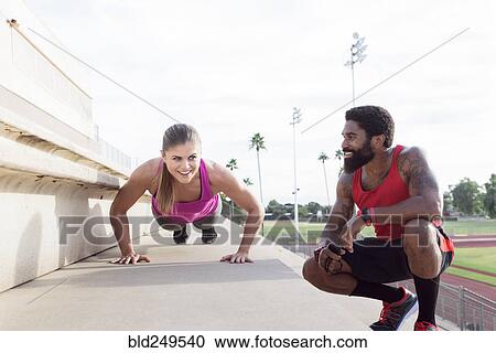 Stock Image - Trainer watching woman do push-ups on bleachers. Fotosearch