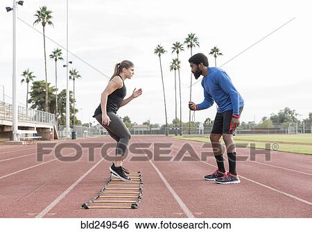 Stock Photograph - Trainer watching woman running ladder. Fotosearch