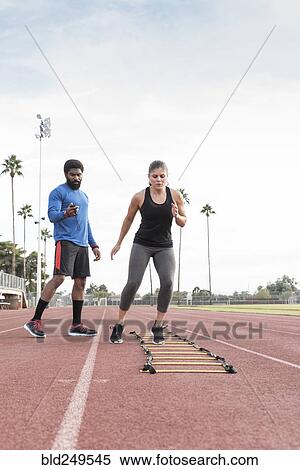 Stock Photography - Trainer watching woman running ladder. Fotosearch