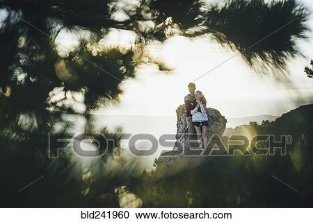 Stock Image - Tree branches framing Caucasian couple hugging at rock. Fotosearch