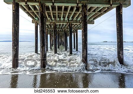 Stock Image - Waves splashing on pilings of wooden pier at beach. Fotosearch
