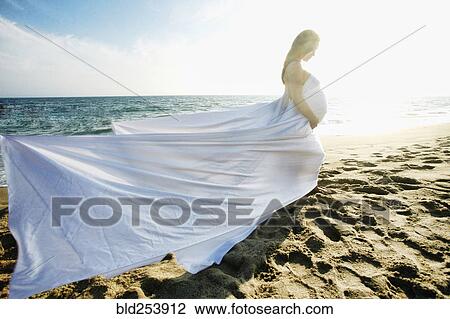 Stock Image - Wind blowing dress of Mixed Race expectant mother at beach. Fotosearch