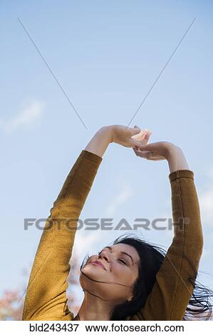 Stock Photo - Wind blowing hair of Caucasian woman with arms raised. Fotosearch