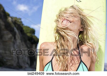 Stock Photo - Wind blowing hair of Caucasian woman holding surfboard. Fotosearch